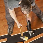 All American Flooring expert installing hardwood floor with mallet and nailer, viewed from above.