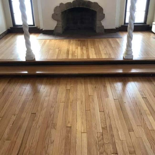 Hardwood floor with two steps, fireplace, and stained finish reflected in a large mirror.