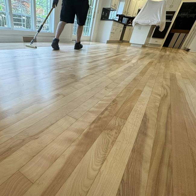 Person refinishing a hardwood floor in a bright, modern kitchen by All American Flooring.