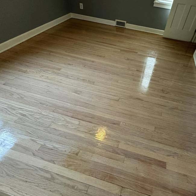 Empty room with All American Flooring, freshly polished hardwood floor, gray walls, and white trim.