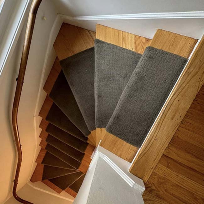 Wooden staircase with dark carpet runners and expert floor refinishing, curving steeply left.