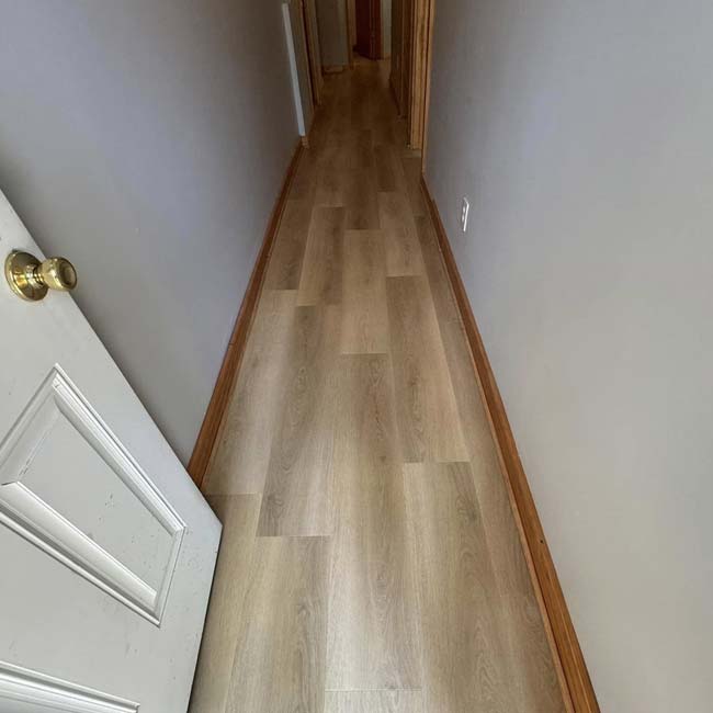 Narrow hallway with hardwood floor installation, beige walls, and a white door partially open.