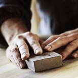 Close-up of hands sanding wood, showcasing expert floor refinishing by All American Flooring.
