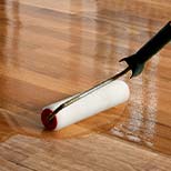 A paint roller applying a clear finish during the floor refinishing process.